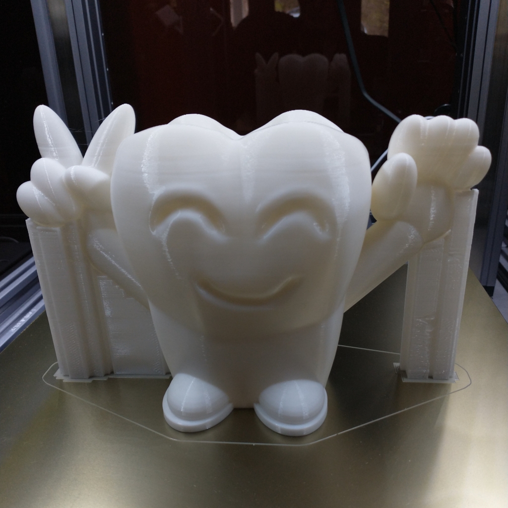 A stylized human tooth with eyebrows and a smile on the face, two raised arms, one showing two fingers as a peace sign, the other waving. Two round feet are at the bottom. Print supports for the arms and hands are visible.