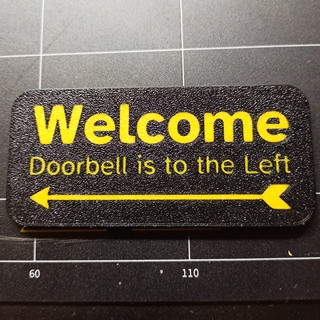 A 3D Printed sign reading "welcome, doorbell is to the left"